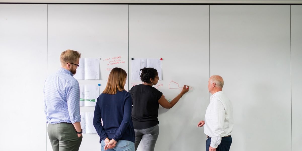 A professional actively explaining or solving a business problem on a whiteboard, demonstrating practical application of skills.